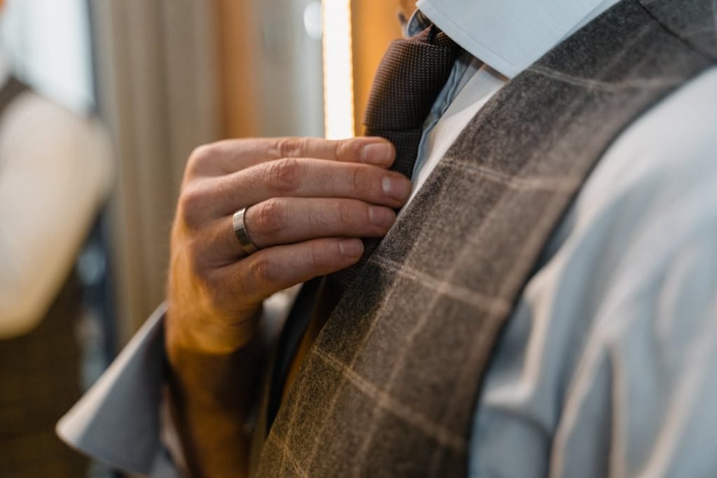 Man adjusting his necktie, wearing a plaid vest. Elegant detail with emphasis on the hand and tie.